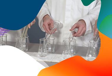 A teacher in a lab coat pours a clear liquid into beakers using a measuring flask