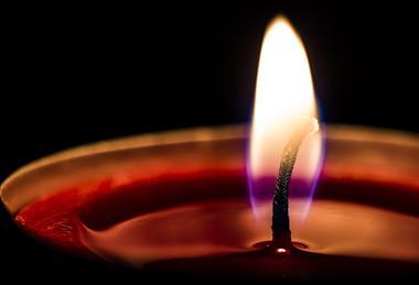 A macro photograph of a lighted candle, showing the flame and a pool of wax around the wick