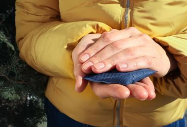 A woman wearing a warm coat outside and holding a chemical hand warmer