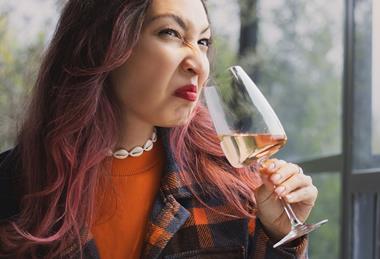A woman pulling a face of disgust as she smells a glass of wine