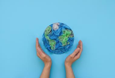 Two hands on either side of a circle of green and blue disposable plastic resembling the Earth