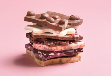 A close-up photograph of pieces of unusual chocolate bars with fruit, nuts and other ingredients in white, milk and dark chocolate