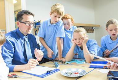 Group of primary pupils watch their teacher do a science demonstration using a candle