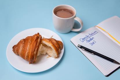 A croissant and a mug of hot chocolate with a pen and notebook which says Chemistry Revision
