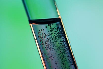 A close-up photograph of a glass test tube containing a liquid with visible air bubbles