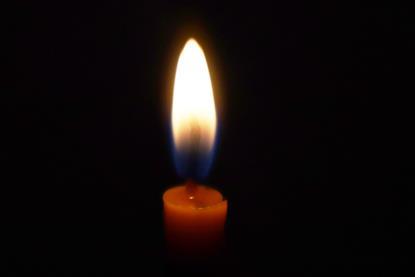 A close-up photograph of the top of a lit candle, showing the flame against a black background