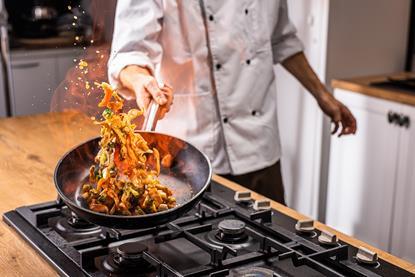 A chef tosses a stir fry with some flames in a frying pan
