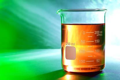 Orange liquid in a glass laboratory beaker against a green-blue background