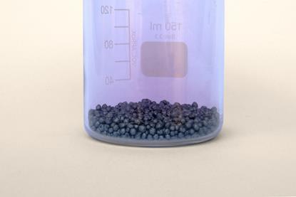 Solid iodine crystals in a glass beaker, with a purple vapour visible as sublimation occurs