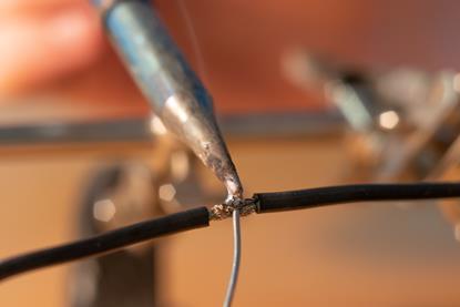 Two black wires being soldered together using a soldering iron