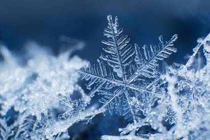 An icy snowflake sitting upright on other snowflakes with a dark navy background 