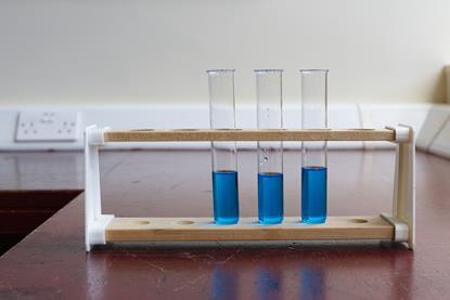 Three glass boiling tubes containing blue copper sulfate solution, resting in a test tube rack on school laboratory bench