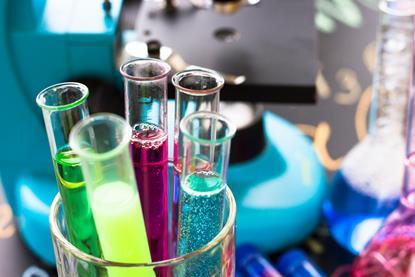 Close up look at test tubes containing a variety of colourful liquids in a beaker and on a busy lab bench 
