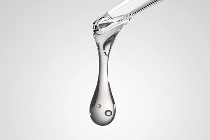 A close-up image of a drop of clear liquid at the tip of a glass pipette