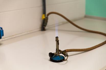A lit Bunsen burner on a laboratory bench, burning with a blue flame