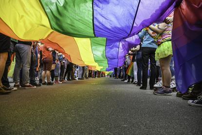 A long rainbow flag being held by two rows of people, seen from below