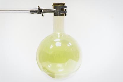 A sealed round-bottom flask suspended using a metal clamp, containing pale green chlorine gas