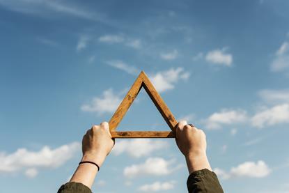 two hands holding a wooden triangle up to a blue sky with clouds in it