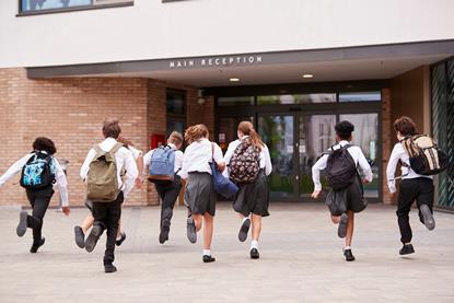 Young high school students in school uniform carrying backpacks run towards the school entrance.