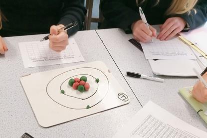 High school students with pens and paper looking at balls of play dough laid out in the shape of an atom