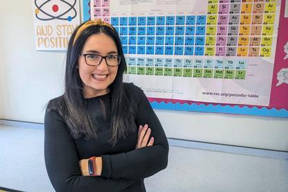 A science teacher standing in front of a periodic table wall poster