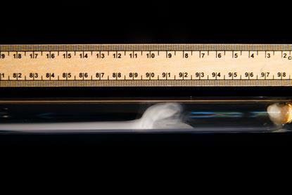 A ruler against a glass tube with smoke forming inside