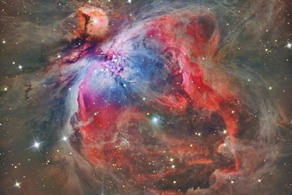 A photograph of the Orion Nebula, showing stars surrounded by a vast interstellar molecular cloud of gas and dust.