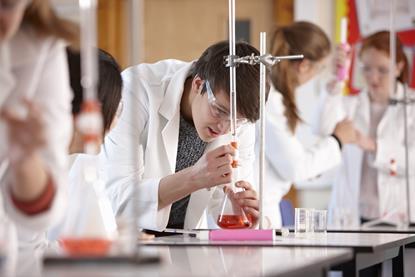 An image showing students doing a titration experiment; the main subject is a male student wearing safety glasses who is focused on his work