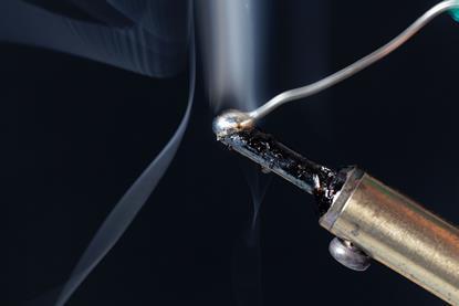 A macro photograph of a length of tin being melted using a soldering iron