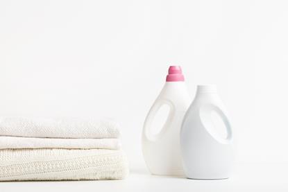 Two white bottles of laundry detergent next to white and cream folded fabrics