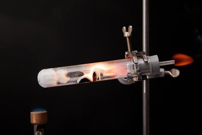 A photo of a heated test tube containing magnesium burning in steam, with another flame burning the hydrogen coming off