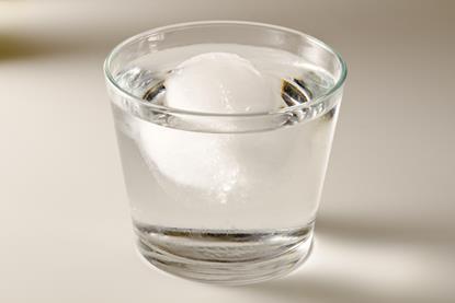 An ice cube floating in a glass of water against a neutral background