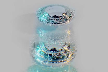 A photo of a metallic drop suspended in a solution and covered in bubbles