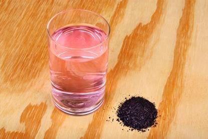 Crystals of potassium permanganate(VII) and a glass of water with a pink-purple hue on a wooden surface