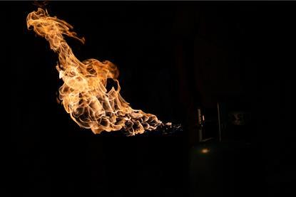 An orange flame shooting from a barely visible gas tank against a dark background