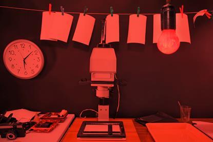 Photographic prints and developing equipment in a dark room lit by a red safelight