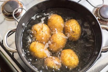 A saucepan on a gas hob with potatoes in boiling water
