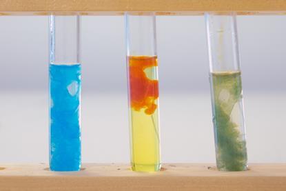 A close-up photograph of three test tubes containing precipitates of blue copper hydroxide, red-orange iron(III) hydroxide and green iron(II) hydroxide