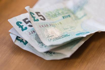 A macro photograph of four paper five pound notes on a wooden surface