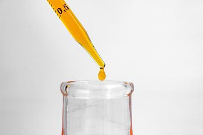 orange drop of liquid falling from pipette into flask