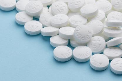 A close-up photograph of a pile of white aspirin pills on a blue paper background