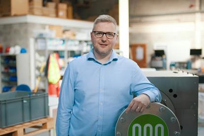 Mike Kenny is smiling at the camera, leaning against a large, metal flow reactor..