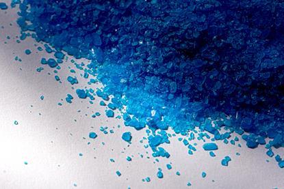A photograph of blue copper sulfate crystals on a white surface
