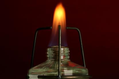 A photograph of a spirit burner and orange-red flame on a black background