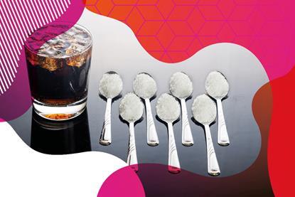 Photo of a glass of cola with ice in. Next to the glass is seven teaspoons with sugar on.