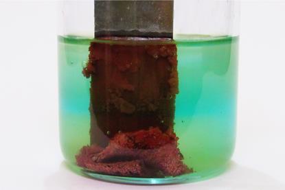 A piece of zinc placed in blue copper sulfate solution in a glass beaker, with a dark coating of copper resulting from the reaction that takes place