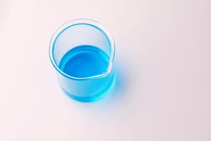 A photograph of a glass beaker containing blue copper(II) sulfate solution on a white surface