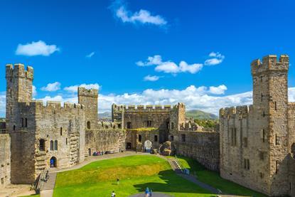 An image of Caernarfon castle with a blue sky and green grass in the castle grounds