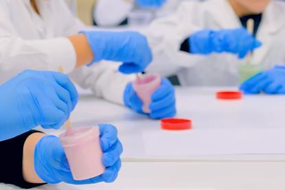 A photograph of students sitting around a table and wearing protective gloves while making slime in plastic pots