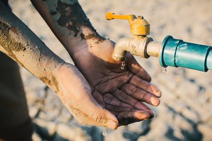 Tap in arid region with hand outstretched waiting for a drop of water 